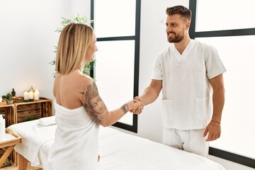 Obraz premium Young caucasian woman at physiotherapy clinic getting muscle massage by professional therapist. Physiotherapist man shaking hands with client