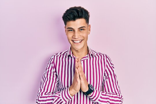 Young hispanic man wearing casual clothes praying with hands together asking for forgiveness smiling confident.