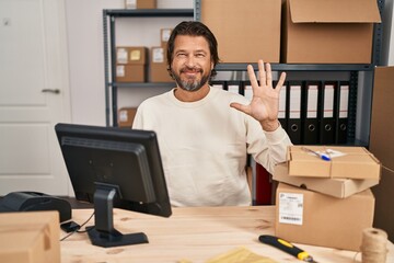 Handsome middle age man working at small business ecommerce showing and pointing up with fingers number five while smiling confident and happy.