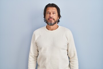 Handsome middle age man wearing casual sweater over blue background relaxed with serious expression...