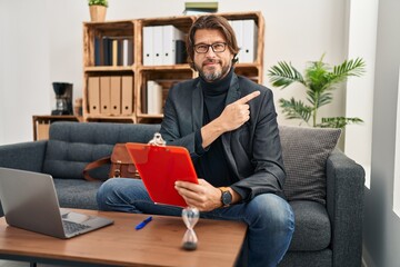 Handsome middle age man working at consultation office pointing with hand finger to the side showing advertisement, serious and calm face