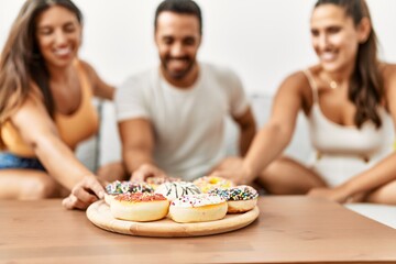 Three hispanic friends smiling happy eating doughnut at home.