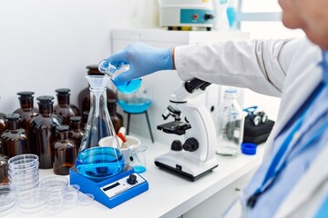 Middle age grey-haired man wearing scientist uniform pouring liquid on test tube at laboratory