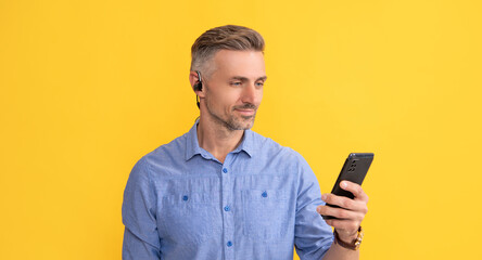 smiling man using phone in headphones on yellow background, communication
