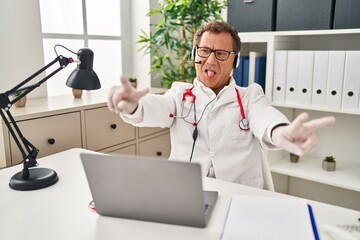 Senior doctor man working on online appointment smiling with tongue out showing fingers of both hands doing victory sign. number two.