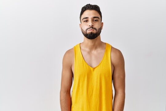 Young handsome man with beard standing over isolated background puffing cheeks with funny face. mouth inflated with air, crazy expression.