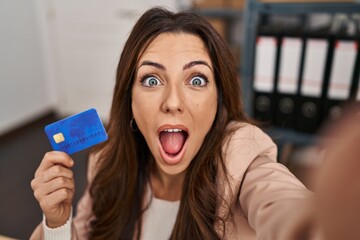 Young brunette woman working at small business ecommerce holding credit card afraid and shocked...