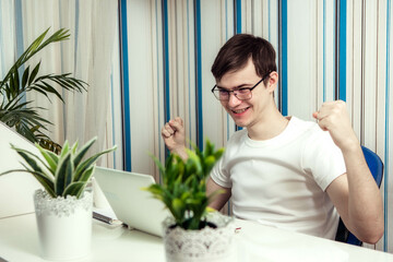 Portrait of a cheerful man, an IT professional working remotely, sitting at a desk and smiling in front of the camera during a break, a human programmer with glasses for vision correction