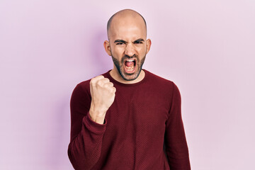 Young bald man wearing casual clothes angry and mad raising fist frustrated and furious while...