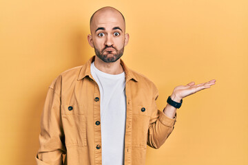 Young bald man presenting with open palms, holding something puffing cheeks with funny face. mouth inflated with air, catching air.