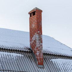 Brick chimney on the roof of a house in the snow