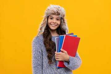 happy kid long hair in hat with copybook on yellow background, education