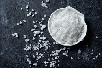 Sea salt in bowl on black background. Coarse salt.