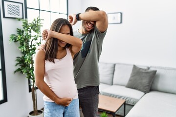Young interracial couple expecting a baby, touching pregnant belly smiling cheerful playing peek a boo with hands showing face. surprised and exited