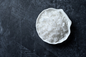 Sea salt in bowl on black background. Coarse salt.