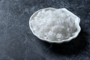 Sea salt in bowl on black background. Coarse salt.