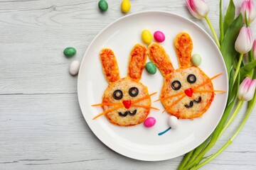 Mini easter bunny pizzas wth chocolate eggs on plate with white wood background.Art food idea for...