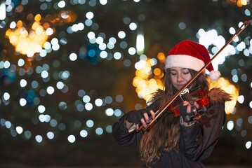 girl playing the violin in front of a Christmas tree. The lights on the Christmas tree are blurred...