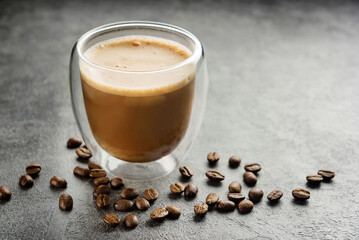 cuppuccino in a double-walled glass cup close-up. A glass of coffee and coffee beans on a dark surface.