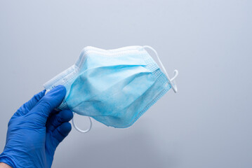 Mano con guantes azules de vinilo sujetando una mascarilla higiénica azul sobre un fondo blanco
