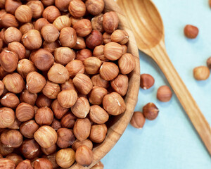 Peeled hazelnuts in a bowl. Near the bowl lies a wooden spoon. Flat lay