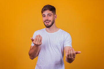 young handsome caucasian man wearing white t-shirt against yellow background inviting to come with hand has a warm smile and friendly expression on his face. happy that you came - obrazy, fototapety, plakaty