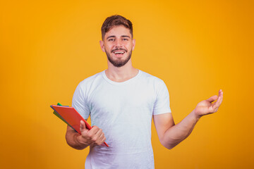 Cute young student boy holding books on yellow background.