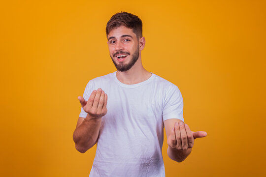 young handsome caucasian man wearing white t-shirt against yellow background inviting to come with hand has a warm smile and friendly expression on his face. happy that you came