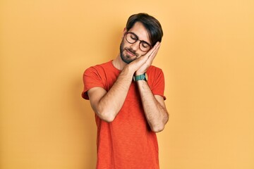 Young hispanic man wearing casual clothes and glasses sleeping tired dreaming and posing with hands...