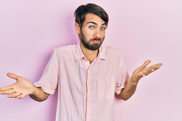 Young hispanic man wearing casual clothes clueless and confused expression with arms and hands...