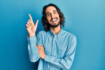 Young hispanic man wearing casual clothes with a big smile on face, pointing with hand and finger to the side looking at the camera.