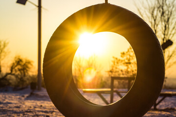 Car tire swing on sunset. Rubber wheel on the rope in the winter evening sun rays. Warm sunset on the kids playground