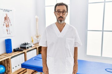 Middle age man with beard working at pain recovery clinic puffing cheeks with funny face. mouth inflated with air, crazy expression.