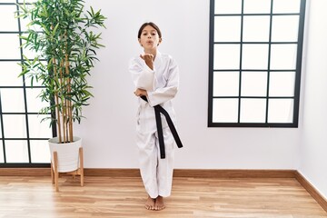 Young hispanic girl wearing karate kimono and black belt looking at the camera blowing a kiss with hand on air being lovely and sexy. love expression. © Krakenimages.com