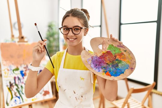 Adorable girl smiling confident holding paintbrush and palette at art studio