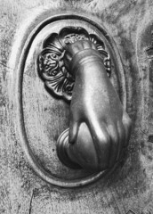 Aldaba de metal antiguo con forma de mano de mujer colocada en una puerta de madera