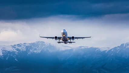 Fototapeta na wymiar A passenger plane takes off on a cloudy day with snowed mountains in the background