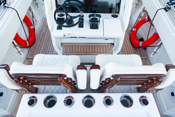 The cockpit of a luxury motorboat, with white leather seats, lifebuoys on the sides and a modern...