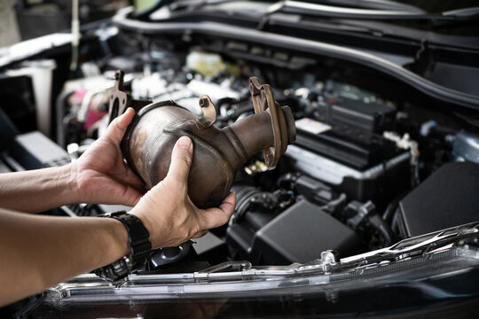 Close up old catalytic converter in hand Technician remove from engine gasoline car dust clogged condition on filter in service concept and engine room in background