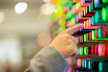 close up female hand choose transparent plastic cylinder form tube from display backdrop showcase wall background,wall of neon colorful acrylic display