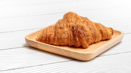 Croissant in wooden plate on vintage white wooden background