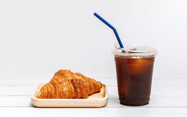 ice americano coffee in a cup with croissant on wooden plate