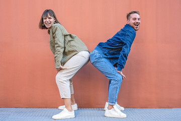 Two happy excited stylish diverse gen z woman and man friends dancing and having fun, trendy outfits people  dancing together isolated on pink wall backgroung, generation z lifestyle