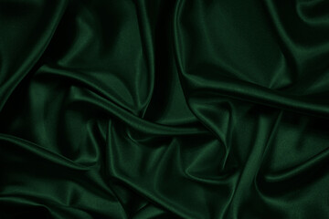 Green background. Folds on shiny fabric surface. Beautiful dark background with space for design. 