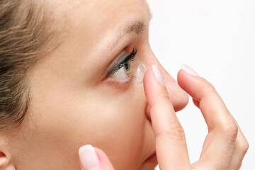 Cropped shot of a young woman applying eye lens with her fingers isolated on a white background. The girl wearing contact lenses. Beauty, vision, ophthalmology