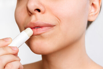 Cropped shot of a young caucasian woman applying a hygienic lipstick on her lips isolated on a white background. Moisturizing chapstick for dry lips. Close up