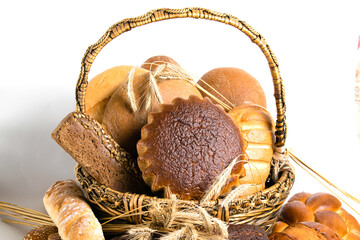 Assorted bread and sweet buns in a basket with spikelets of wheat on a white background