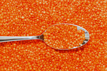 Red lentils scattered close-up with a spoon.