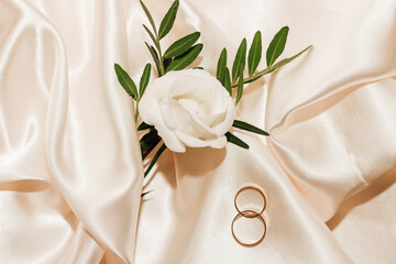 Floral boutonniere with wedding bands on a silk background, space for text.