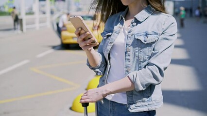 Unrecognizable woman tourist with suitcase by asphalt road waiting for taxi under bright summer sunlight. Lady using app on smartphone for Taxi Hailing in airport